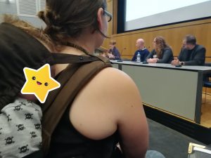 baby sleeps on mothers back in front of conference panel