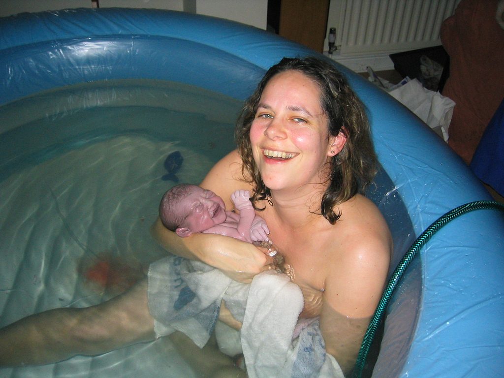 smiling new mother holding baby in birthing pool